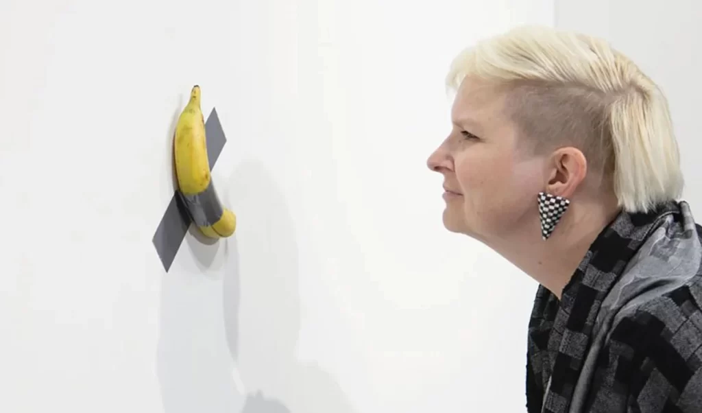 Woman looking at a banana duct taped to a wall 