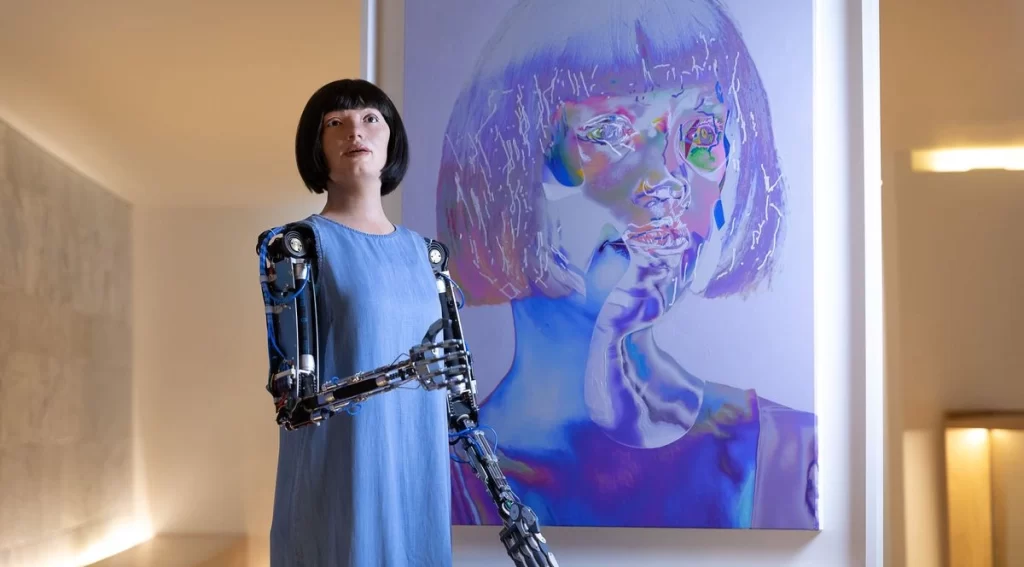 Robot Ai-Da standing infront of her self-portrait 